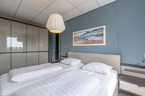A hotel room with a bed, a bedside table, a lamp, and a painting of a beach scene.