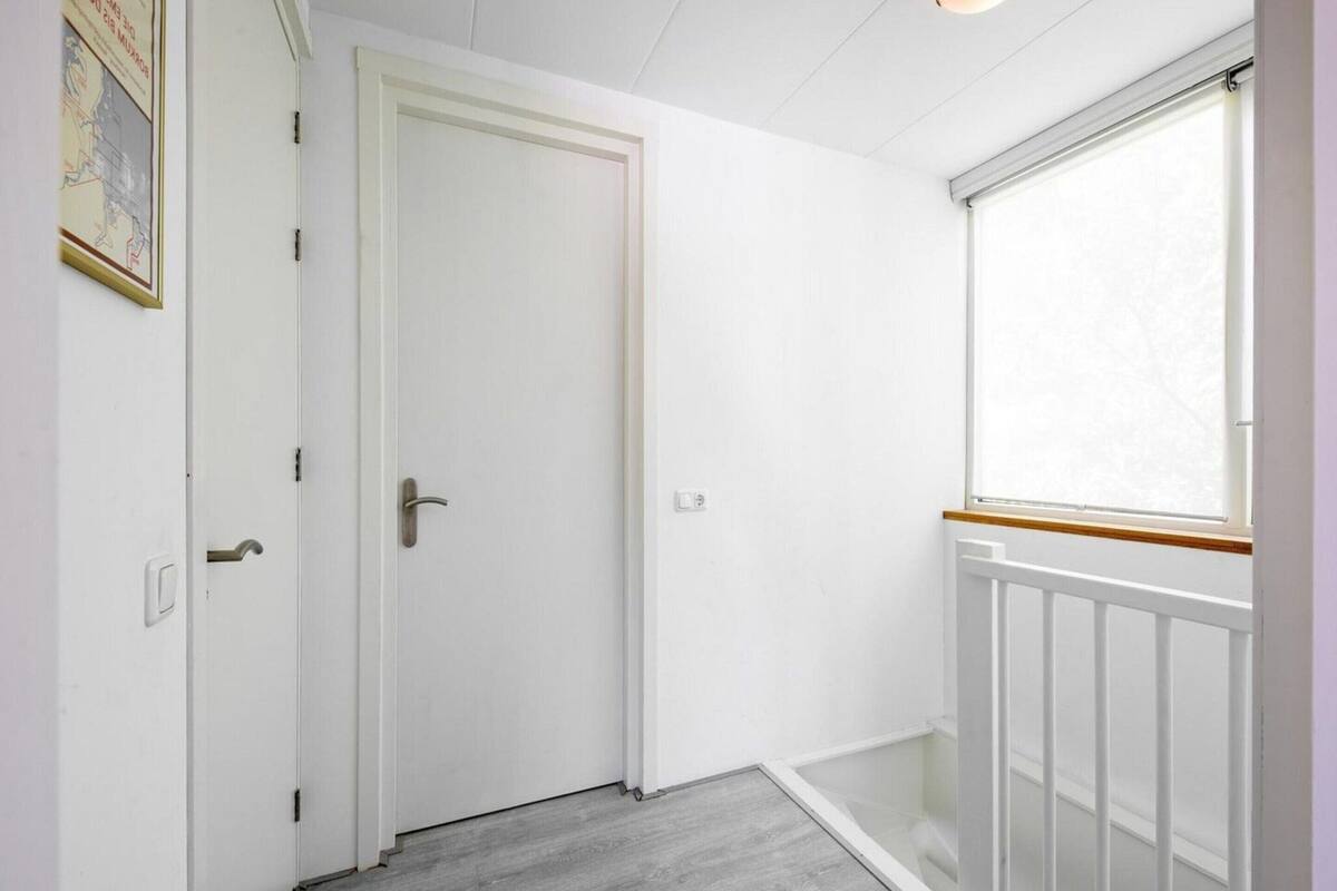 A narrow hallway with a white door, a window with a wooden frame, and a light switch on the wall.