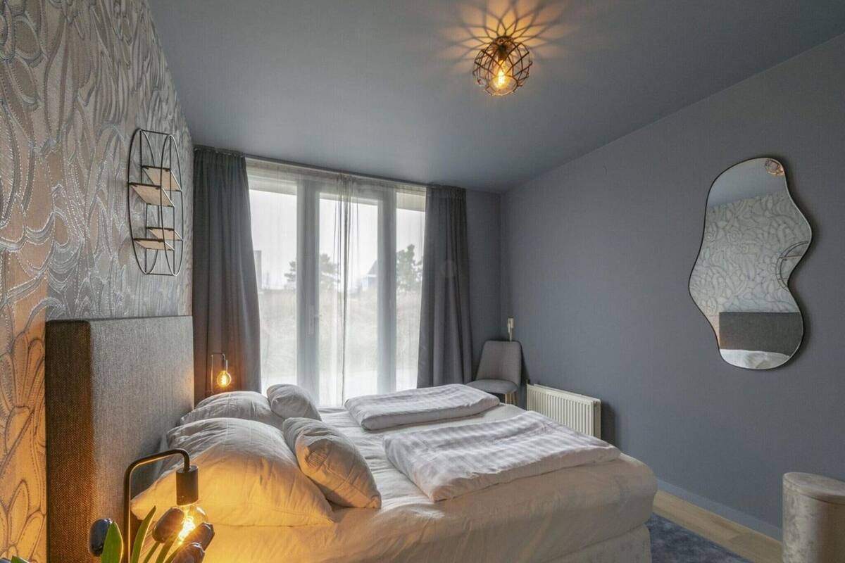 A bedroom with a bed, a radiator, a mirror, and a window with curtains.