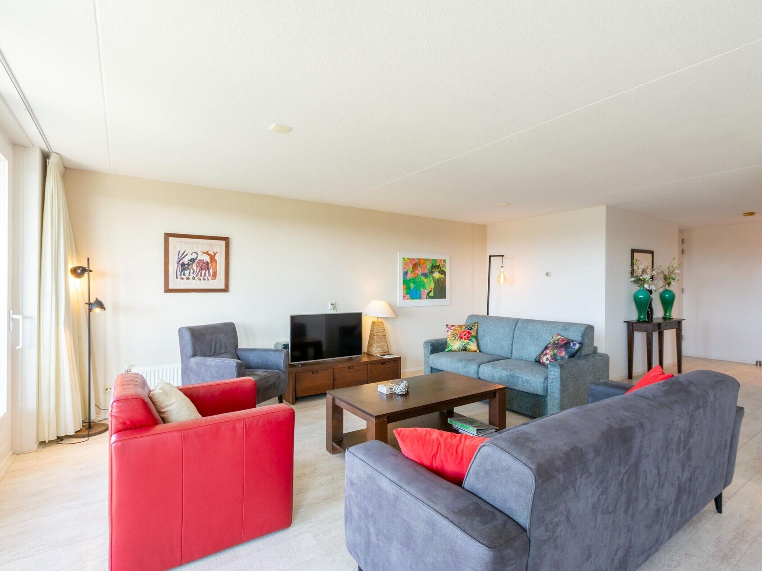A living room with a grey sofa, a red sofa, a coffee table, and a TV. There are two paintings on the wall and a floor lamp.