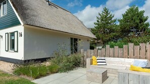 Ein Haus mit einem Strohdach, einem Holzzaun und einer Terrasse mit einer Bank und Kissen.
