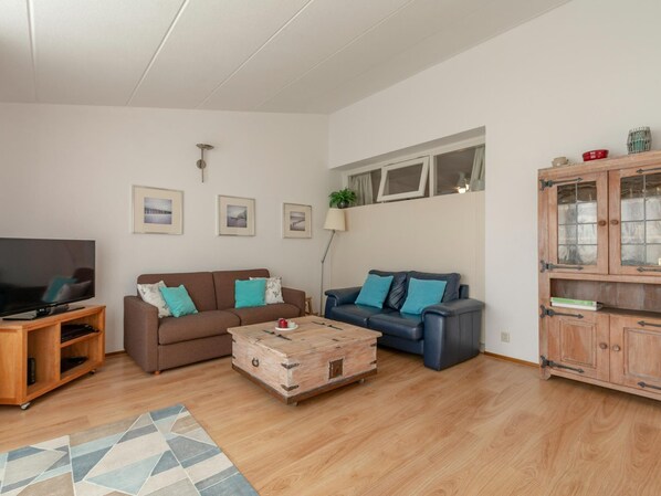 A living room with a brown sofa, a blue sofa, a wooden coffee table, a TV on a wooden stand, and a cabinet with glass doors. - The Lovely Apartment is Beautifully Decorated (Julianadorp)