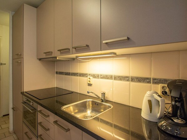A modern kitchen with a stainless steel sink, a kettle, and a coffee maker on the counter. - The Lovely Apartment is Beautifully Decorated (Julianadorp)