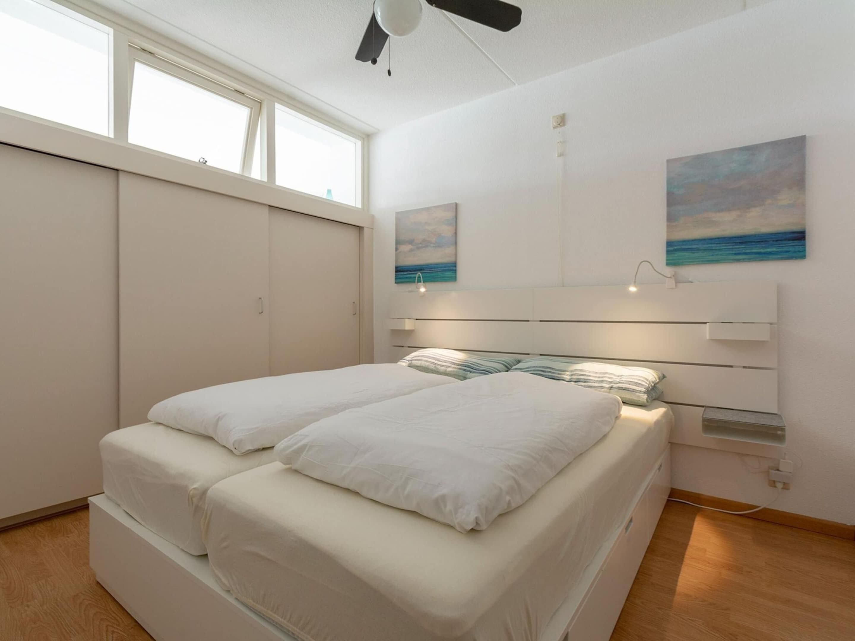 A modern bedroom with a bed, a ceiling fan, and artwork on the walls.