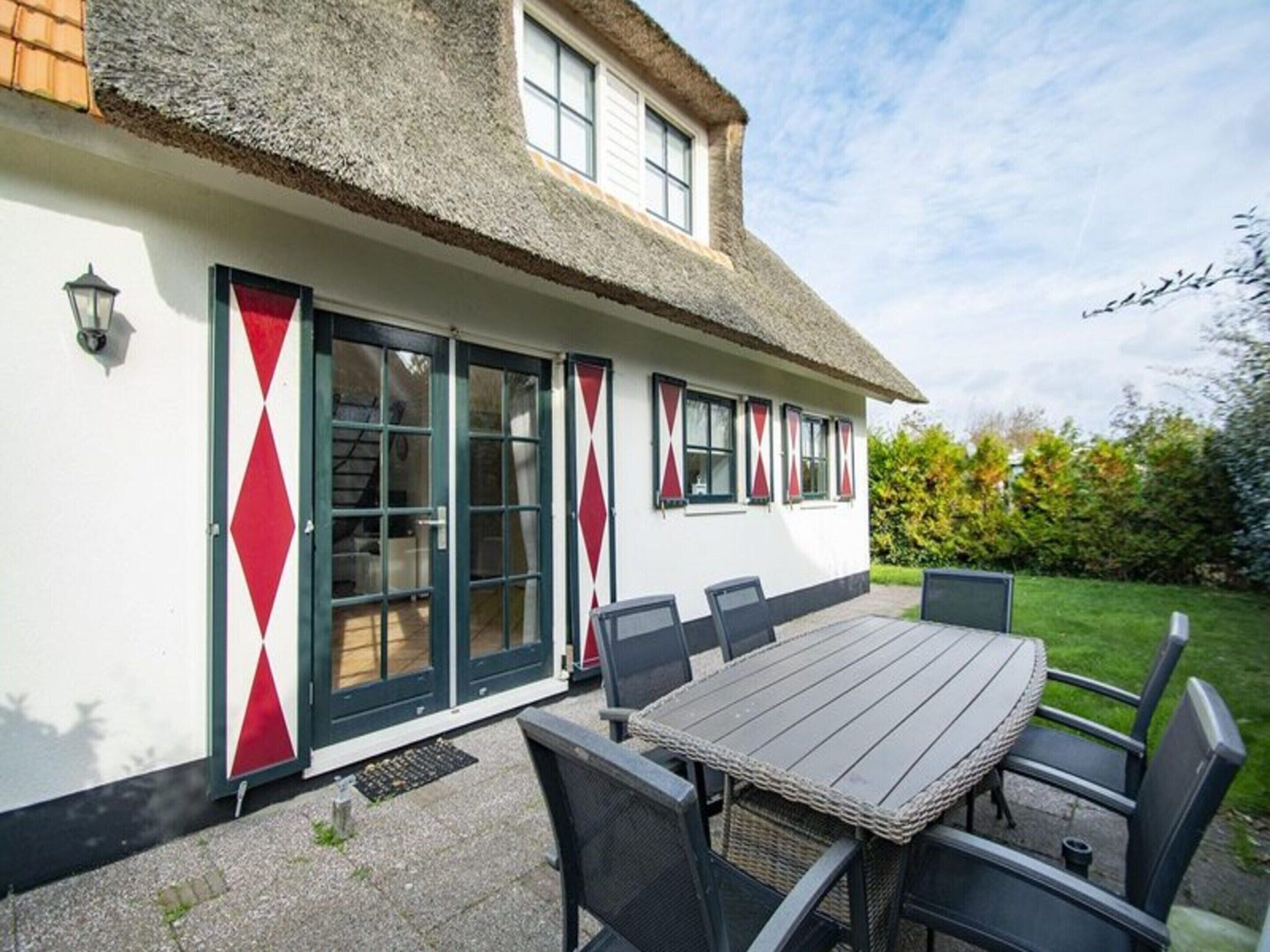 A house with a thatched roof, white exterior walls, and a dining area with a table and chairs.