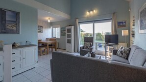 A spacious living area with a sofa, a dining table, and a kitchen area with cabinets. - Ooghduyne 149, Villa Near Beach (Julianadorp)