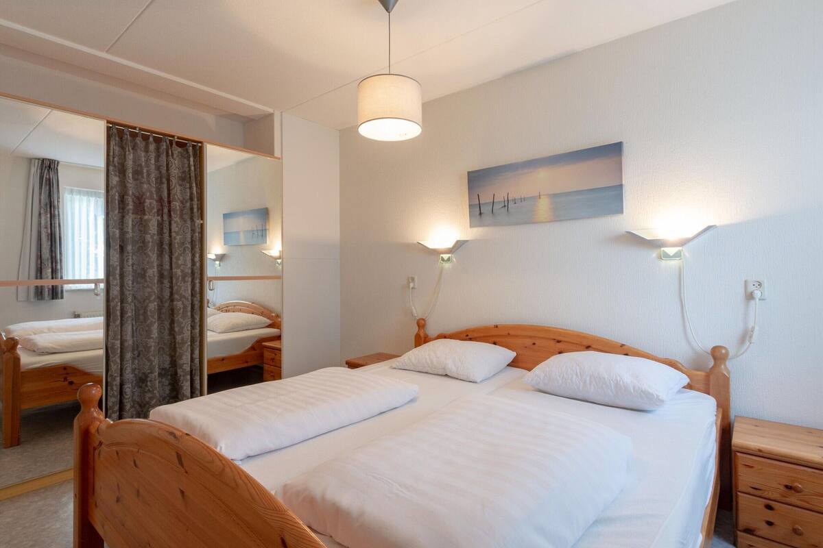 Ein Hotelzimmer mit Doppelbett, Holz-Kopfteil, zwei Nachttischen, einem Spiegel, einem Bild an der Wand und einer Deckenleuchte.