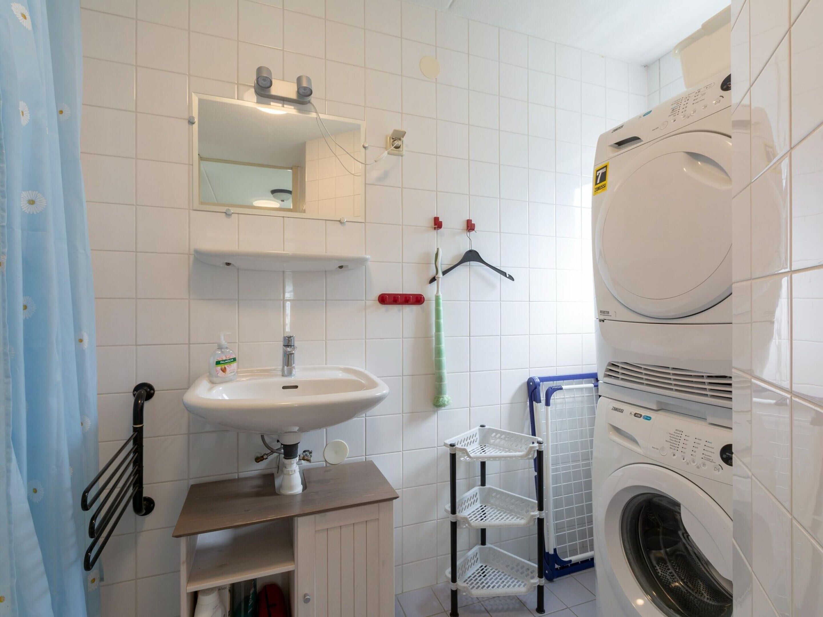 Ett badrum med handfat, spegel, tandborsthållare och en tvättmaskin.