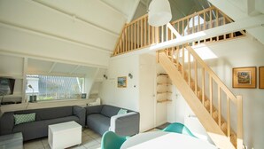 Una sala de estar moderna con un sofá seccional, una mesa de centro blanca, sillas color turquesa, una escalera de madera y un techo blanco.
