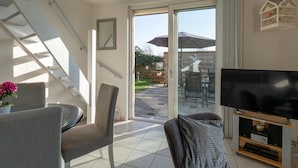 A modern living room with a flat-screen TV, a dining table with chairs, a staircase, and a sliding glass door leading to an outdoor area. - Klaproos, Holiday Home (Callantsoog)