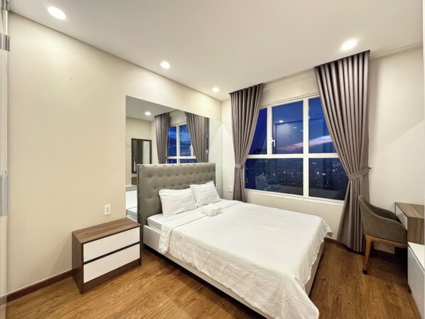 A modern bedroom with a large bed, a bedside table, a mirror, and a window with curtains.