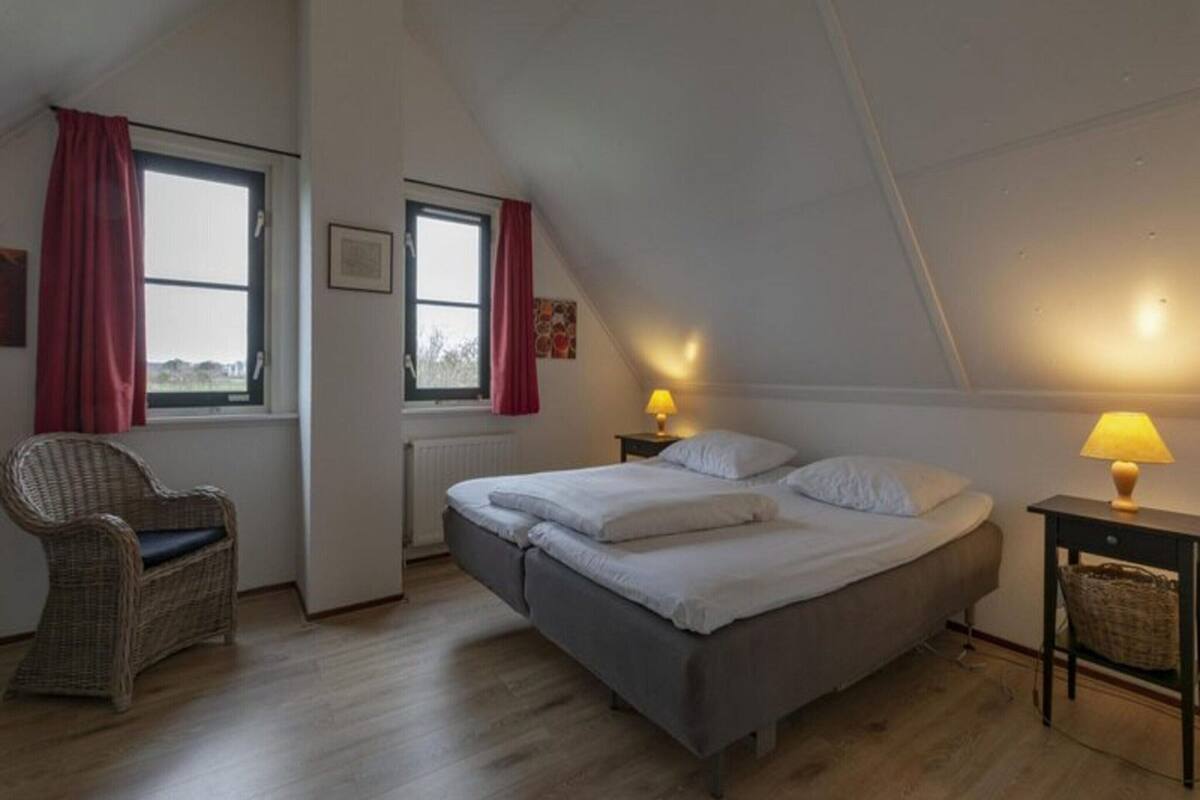 A bedroom with a bed, two bedside lamps, a chair, and a window with curtains.