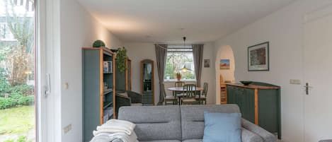 En hyggelig stue med en grå sofa, et spisebord med stole, en reol og et køkkenområde.