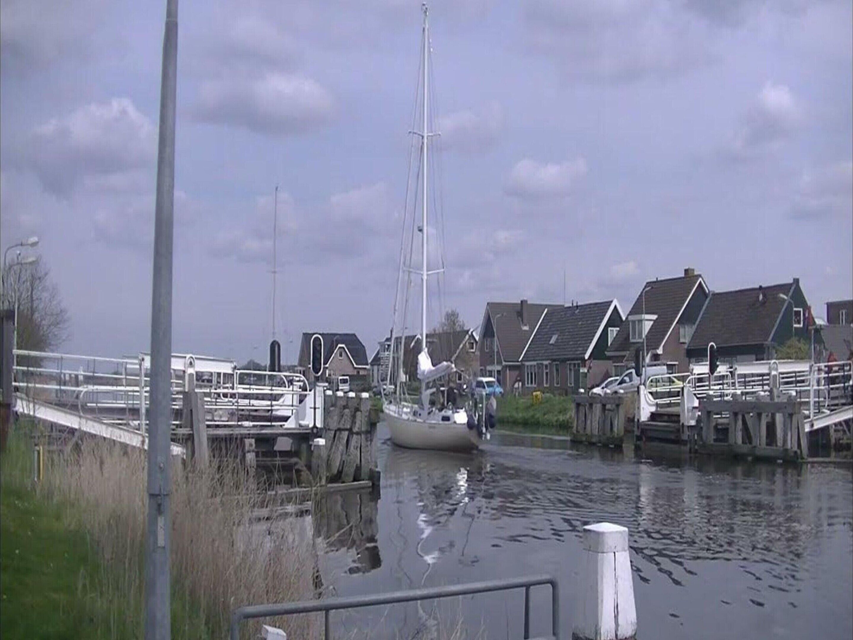 A marina with a sailboat docked, surrounded by houses and a wooden walkway.