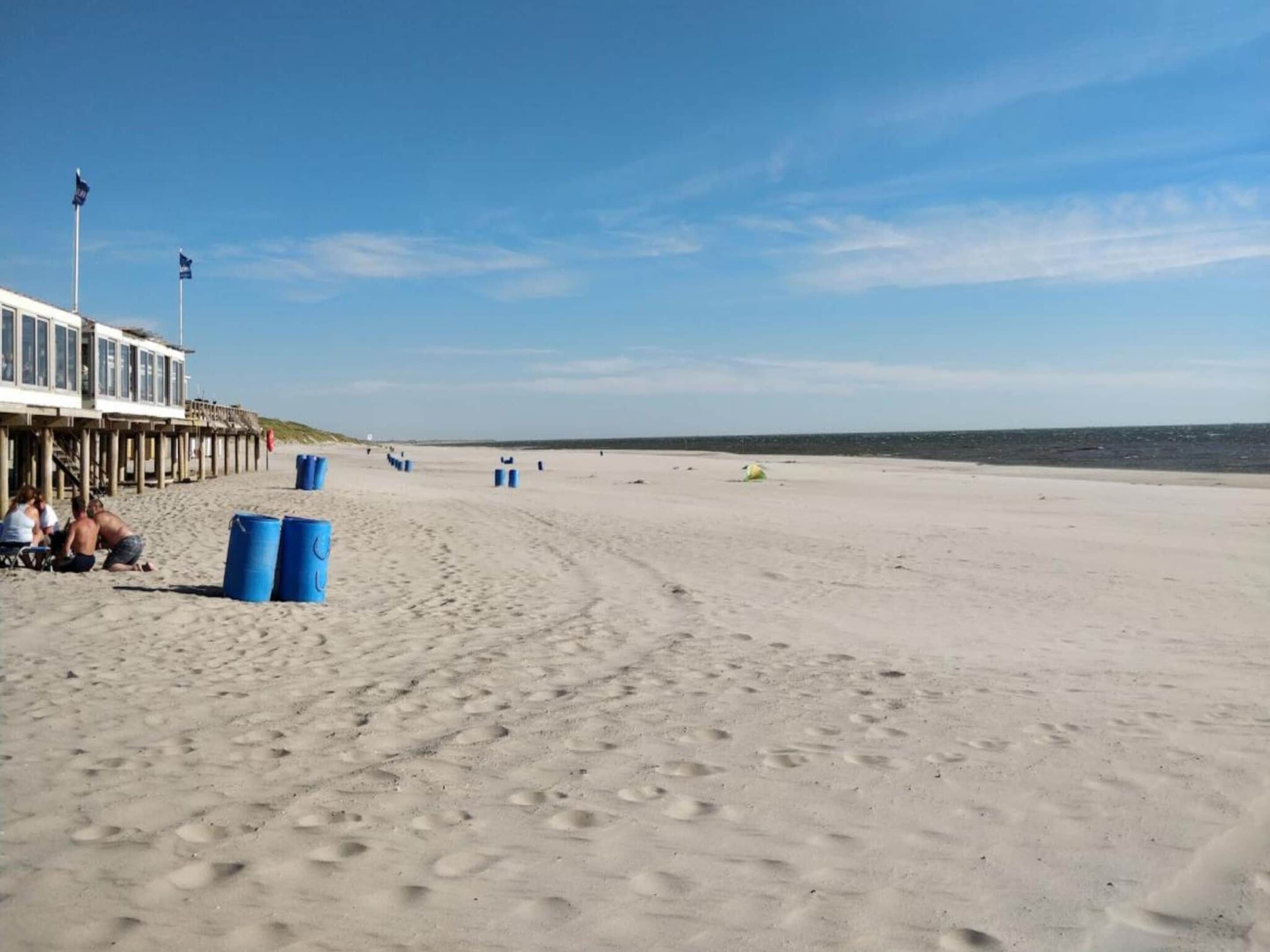 Une plage avec une jetée en bois, des barils bleus et des empreintes de pas dans le sable.