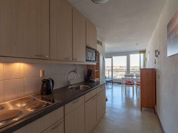 Enjoy a kitchen with light cabinetry, stainless steel sink, and microwave, opening to a balcony with a view of the surrounding landscape.