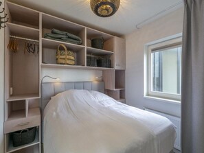 Cozy retreat with a neatly made bed, wardrobe, and comfortable seating area.