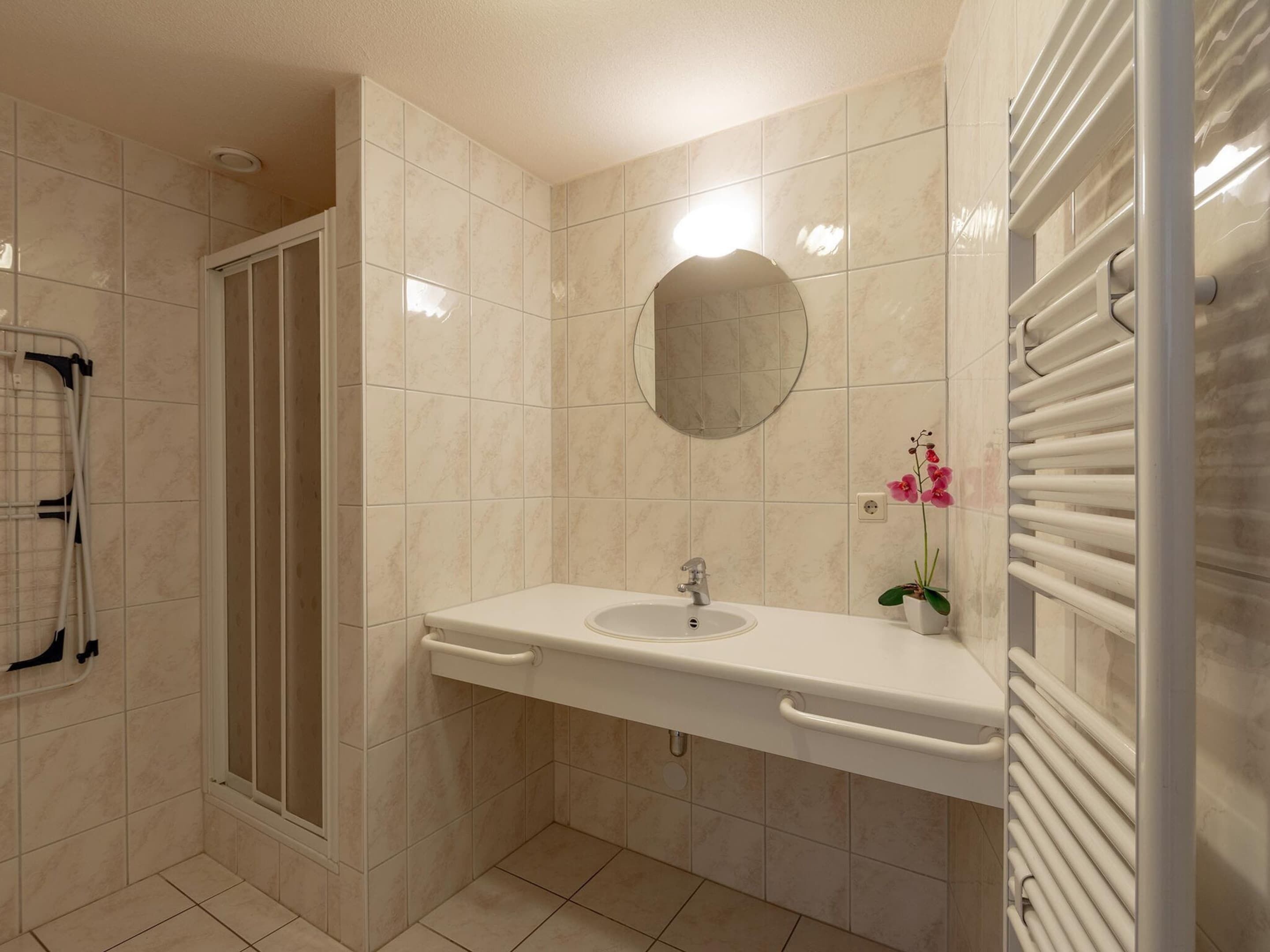 A bathroom with a shower, a sink, a mirror, and a radiator.