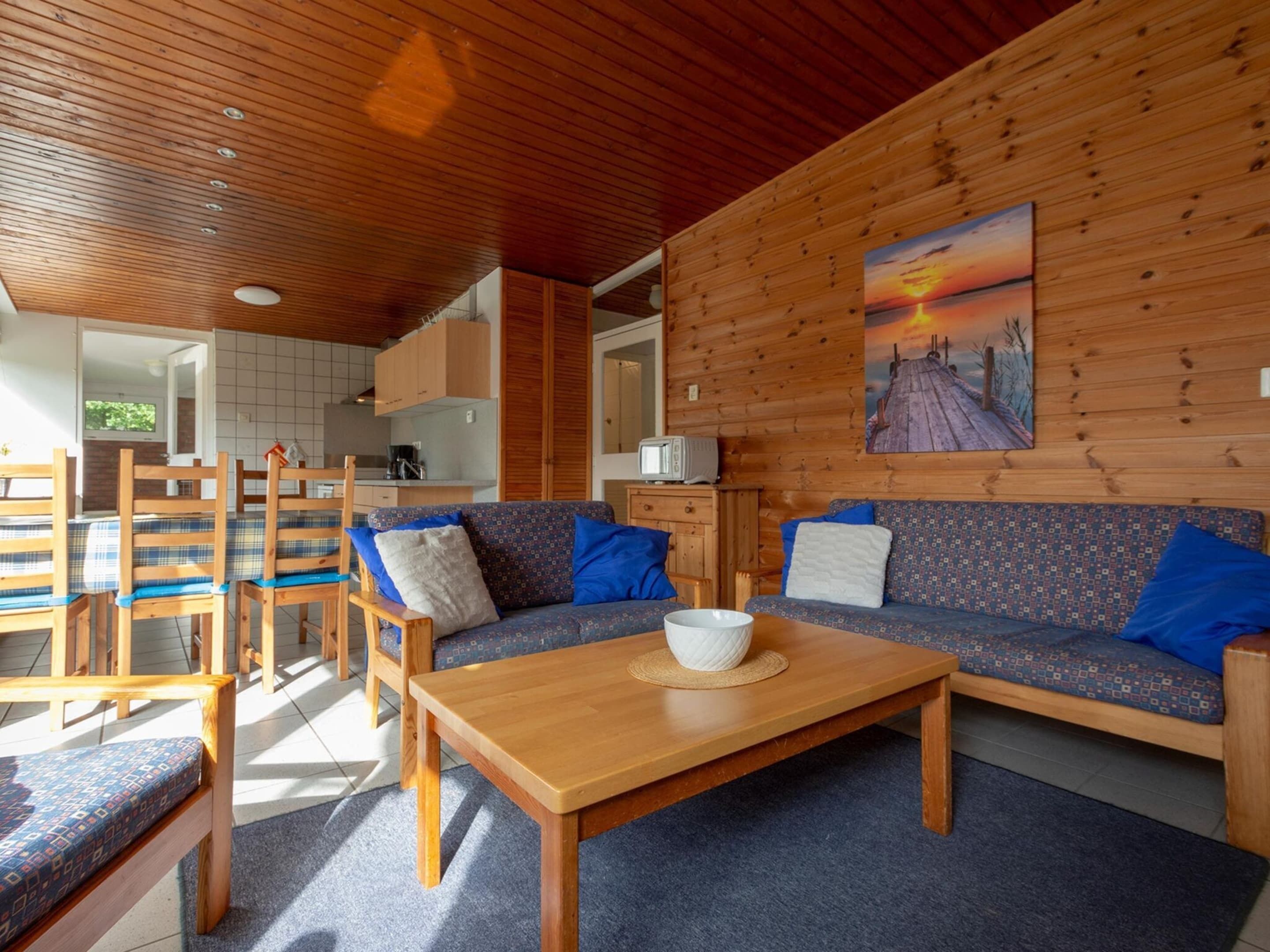 A cozy living area with a wooden ceiling, a sofa with patterned cushions, a coffee table, and a painting of a sunset.