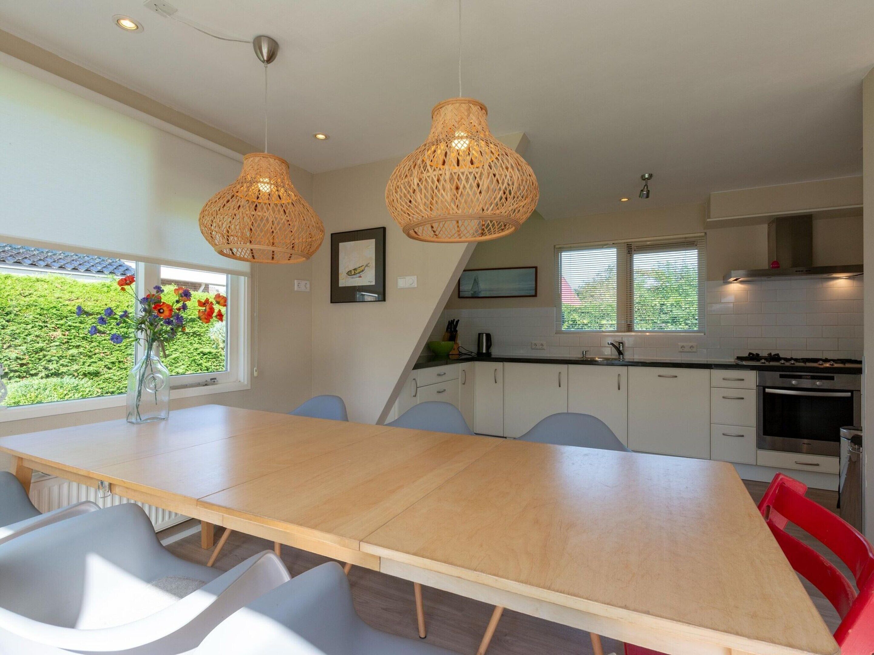 A modern kitchen with white cabinets, a wooden dining table, and two hanging wicker chandeliers.