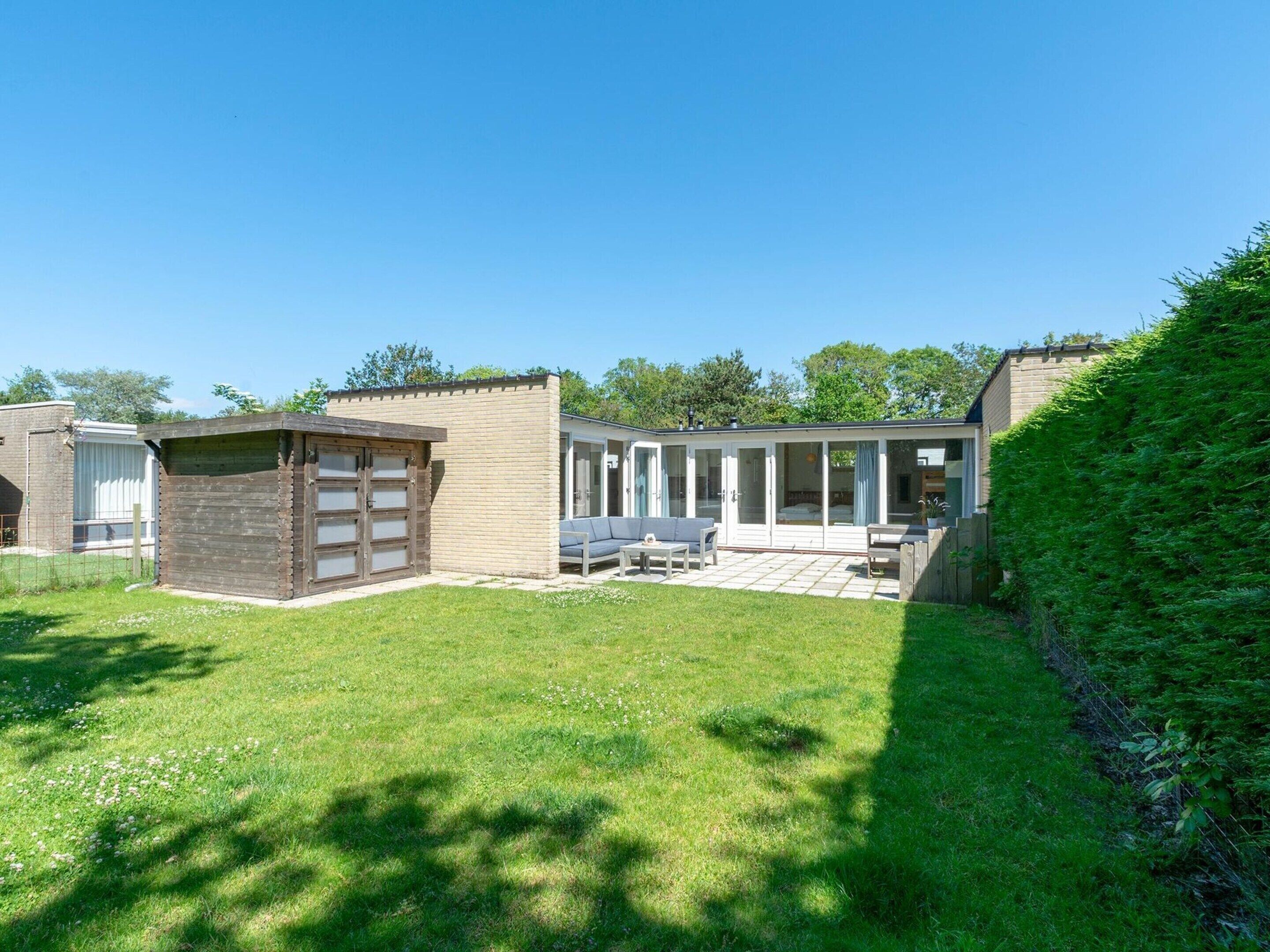 A small, single-story building with a garage, a patio area with outdoor furniture, and a large windowed room.