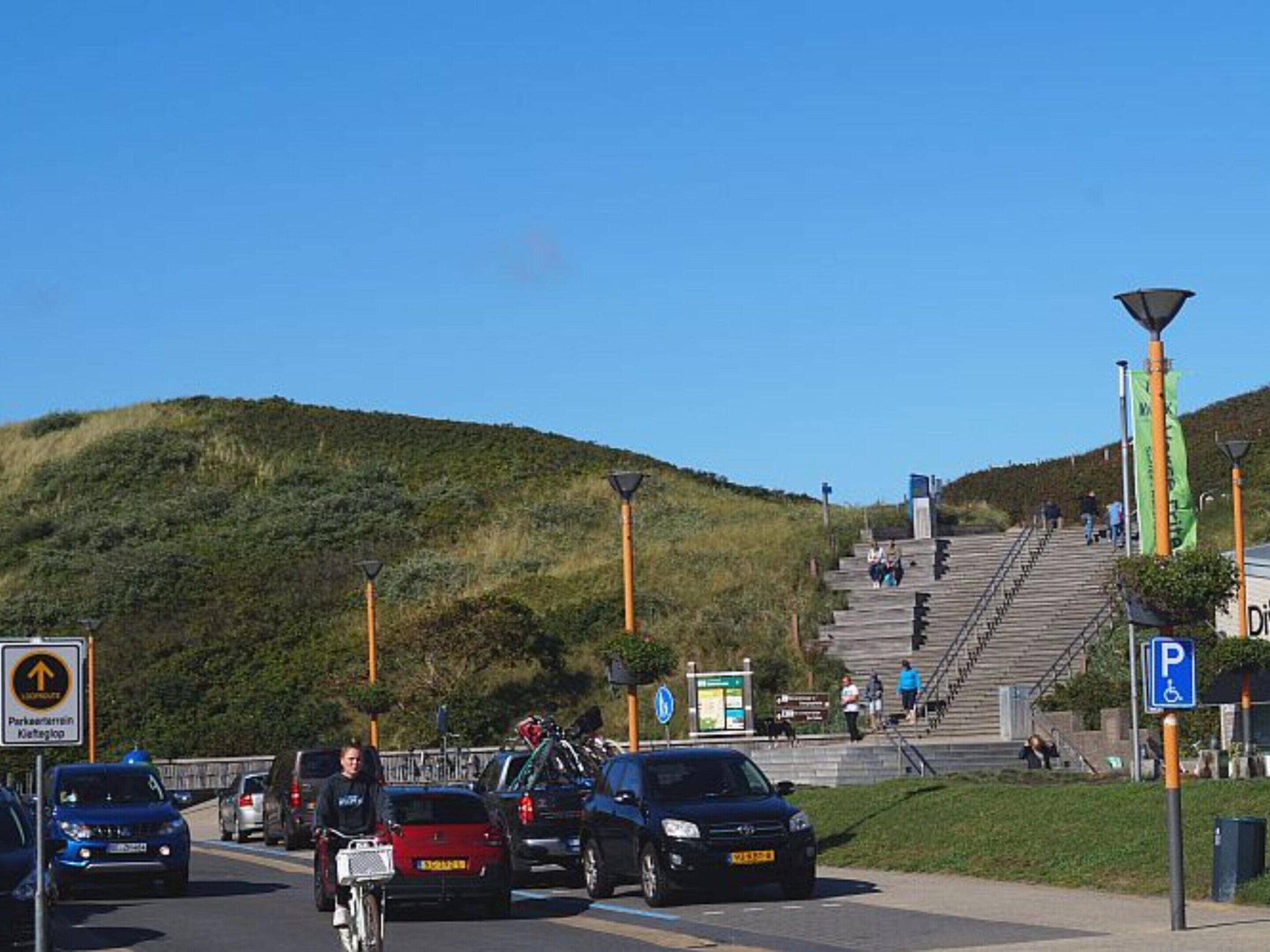 A parking area with a sign indicating a parking lot and a pedestrian pathway leading up a hill.