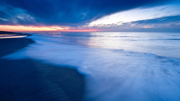 Una playa con mar tranquilo y cielo al atardecer.