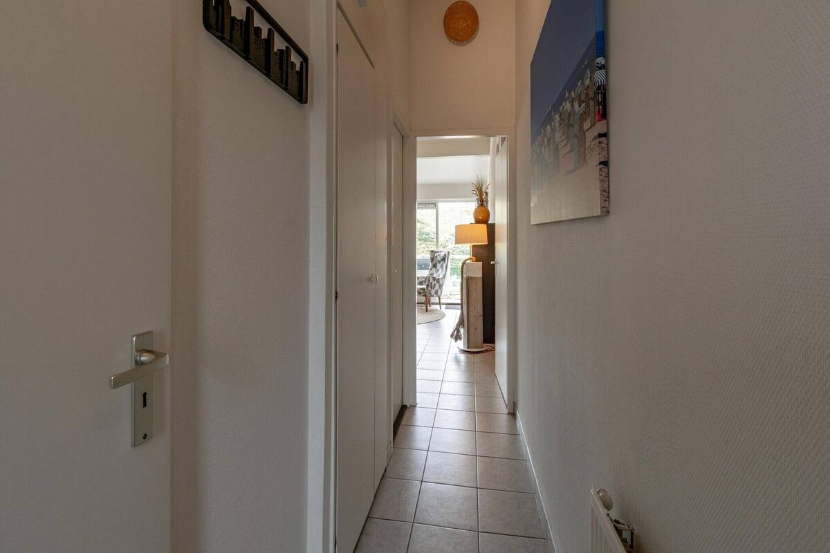 A hallway with a door on the left, a lamp, and a chair in the distance.