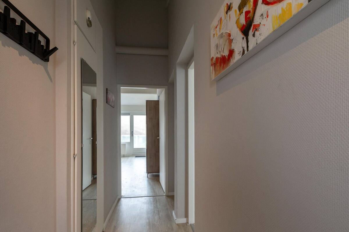 A hallway with a wooden floor, white walls, and a door leading to another room.