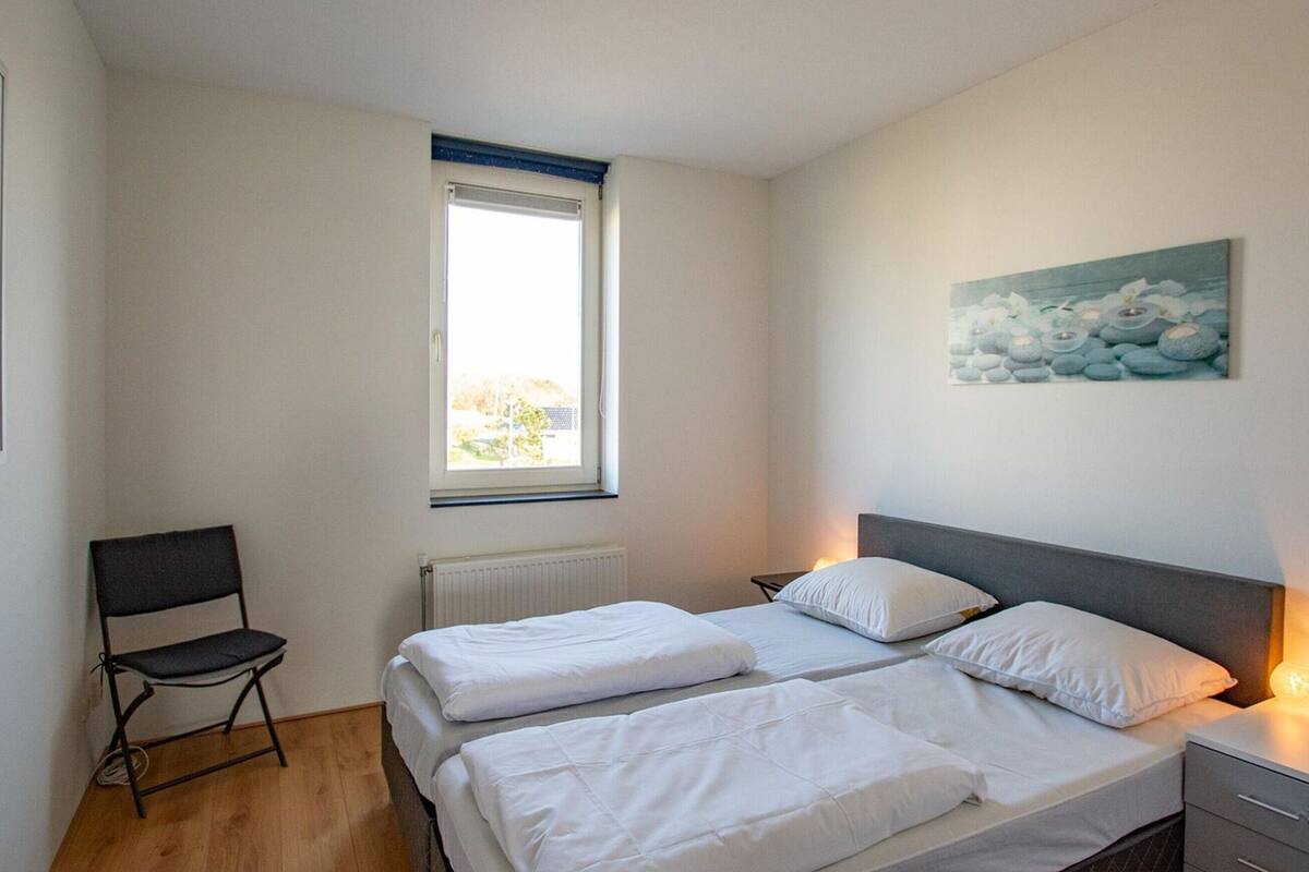 A room with two beds, a chair, a radiator, a window, and a painting on the wall.