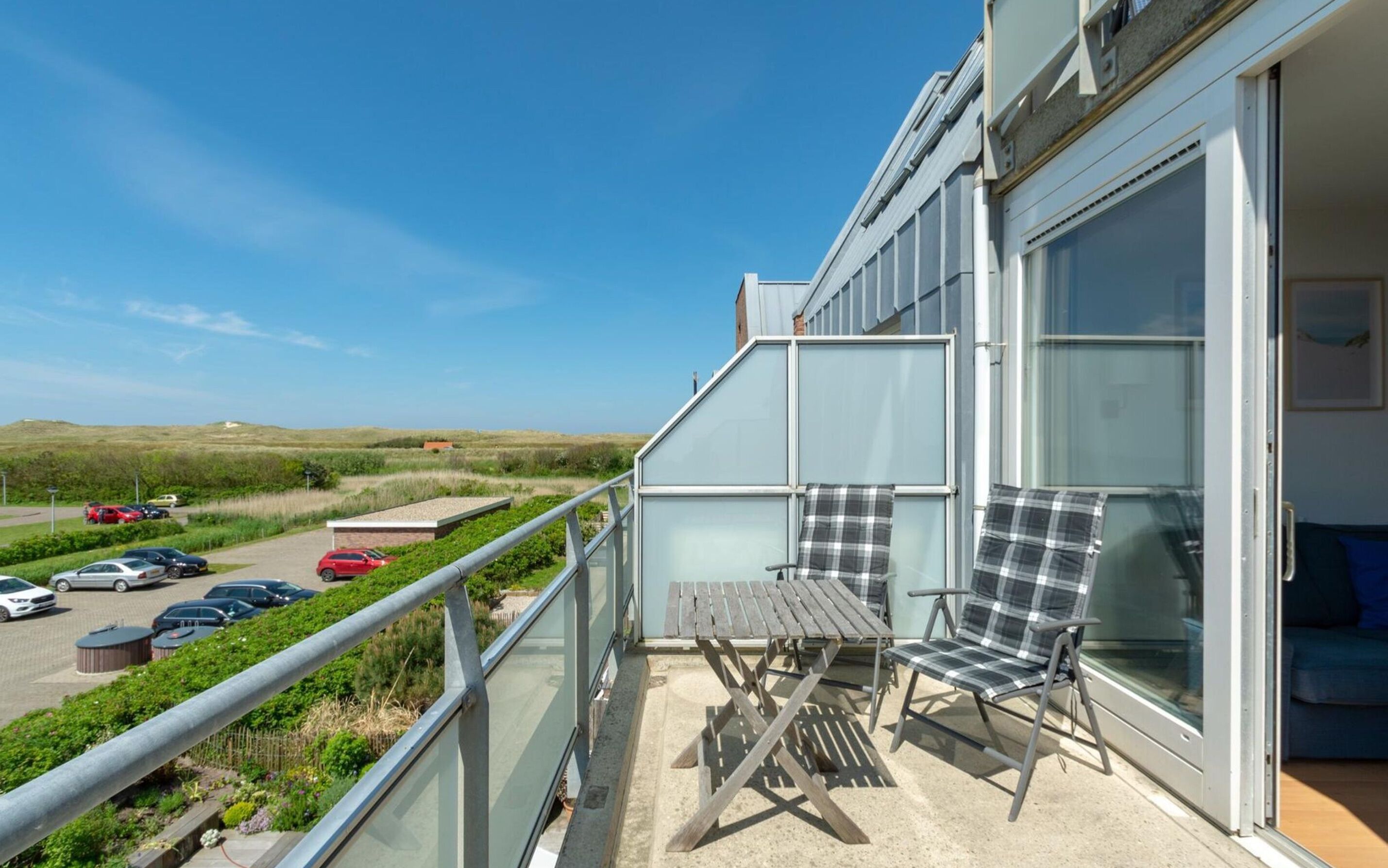 Un balcon avec une table et deux chaises, donnant sur un parking et un paysage verdoyant.