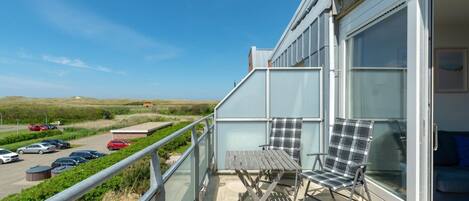 Un balcon avec une table et deux chaises, donnant sur un parking et un paysage verdoyant.