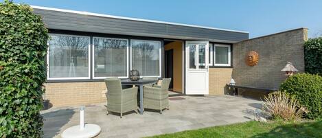 A modern house with a patio, a dining table, and chairs.