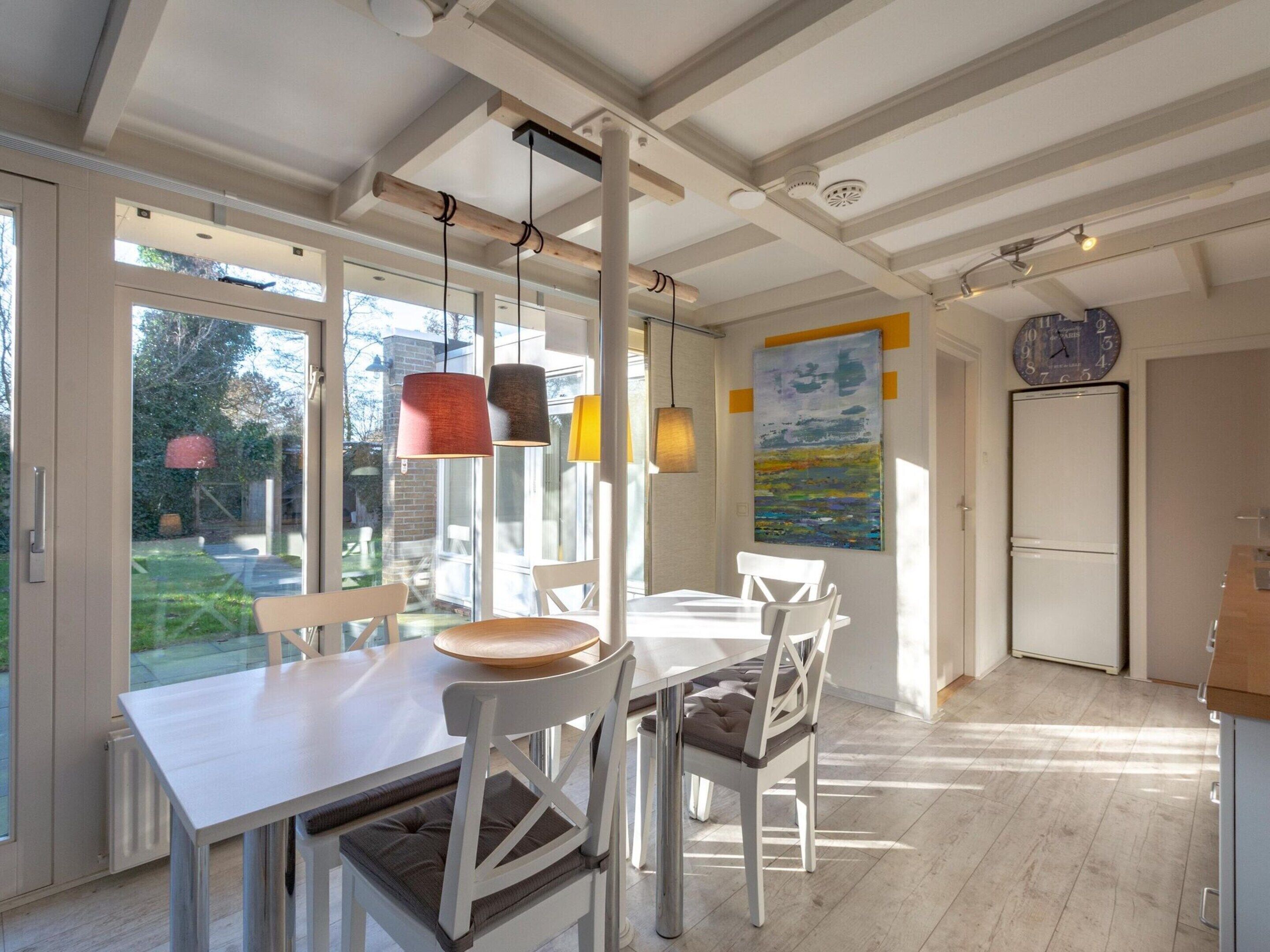 A dining area with a white table and chairs, pendant lights, and a view of the outdoors.