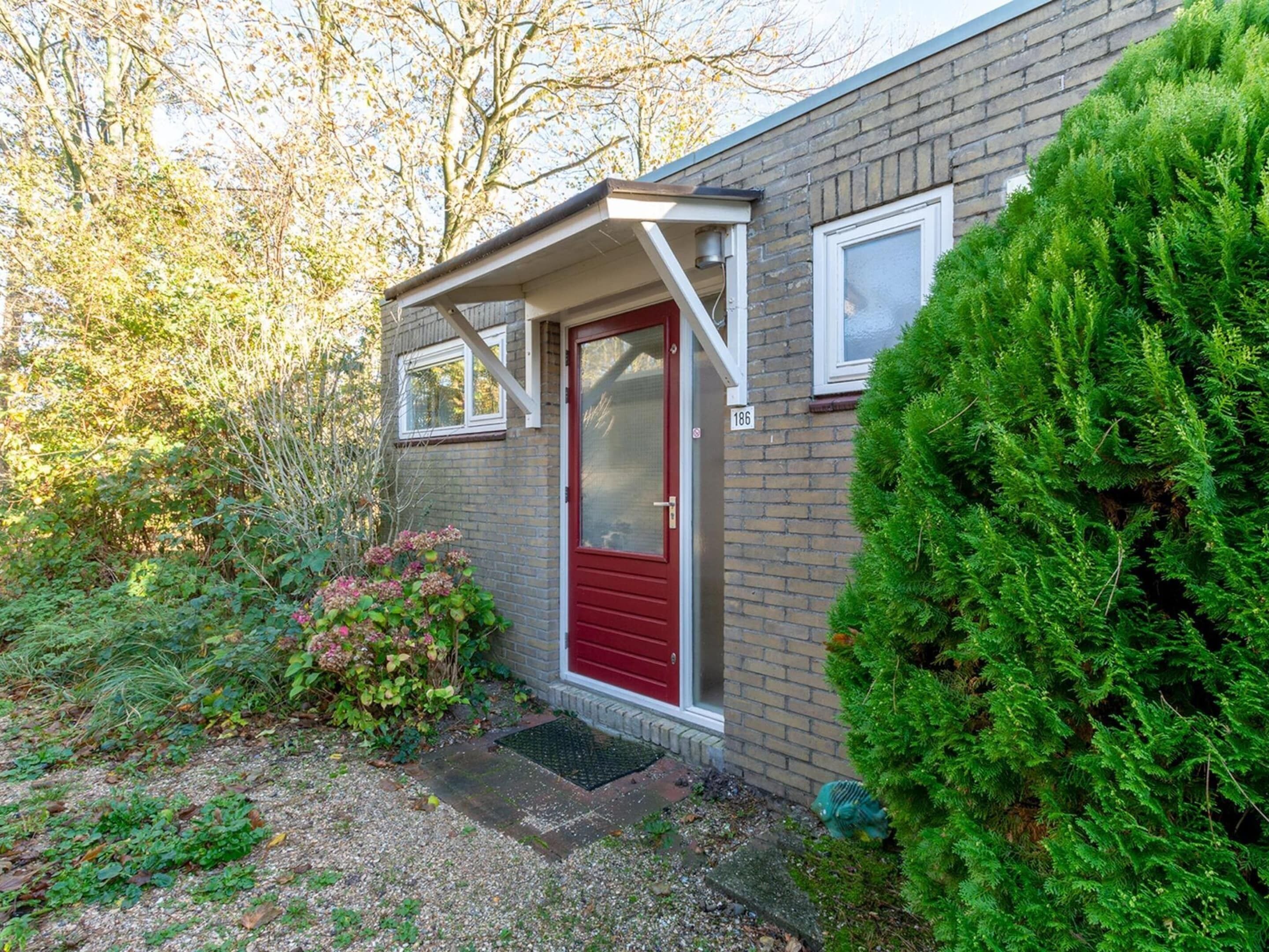 A brick house with a red door, a small porch, and a well-maintained garden.