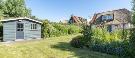 A residential area with a small shed, a house with a thatched roof, and a well-maintained lawn.