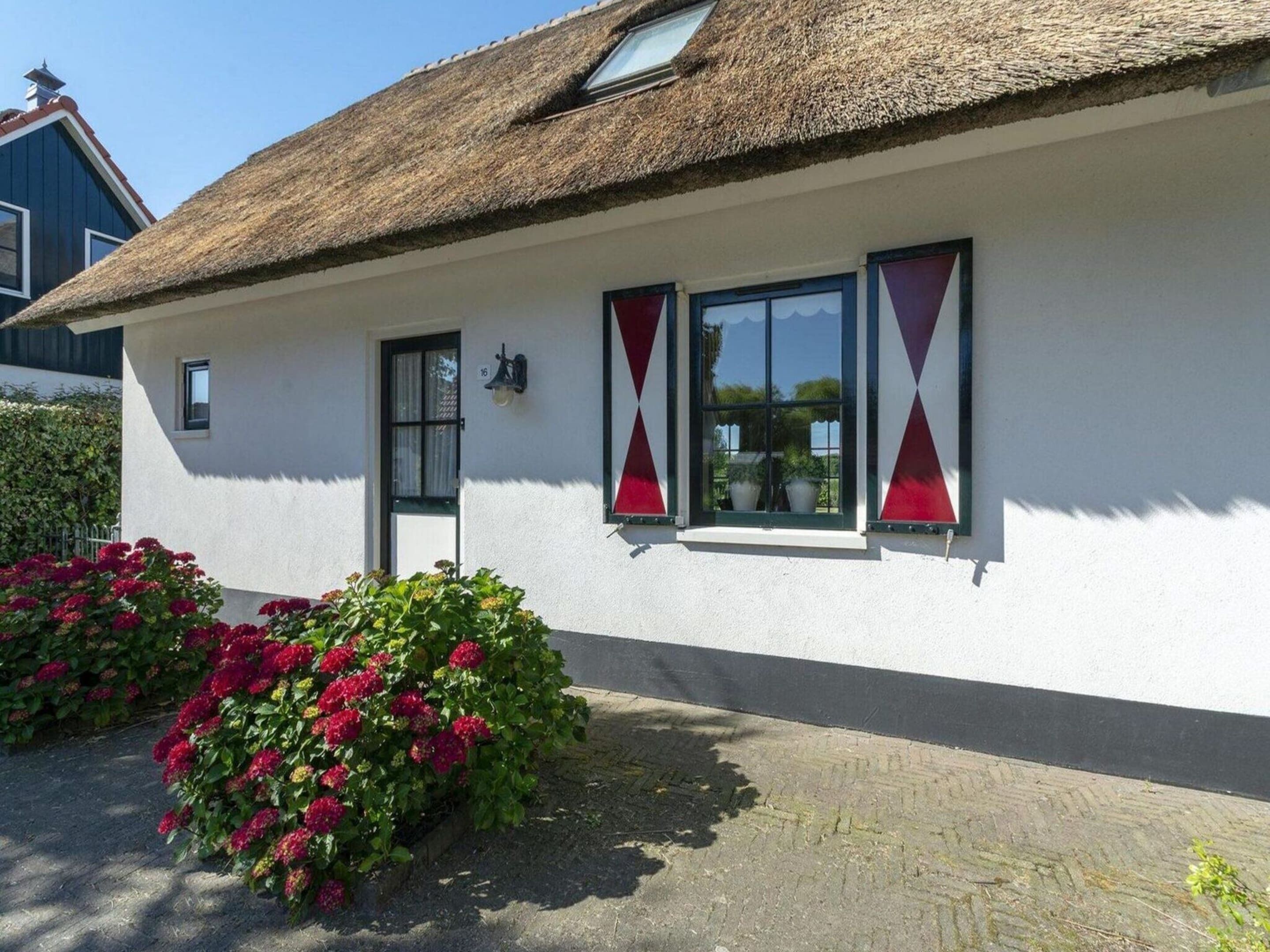 A white building with a thatched roof, a small door, and two windows with red curtains.