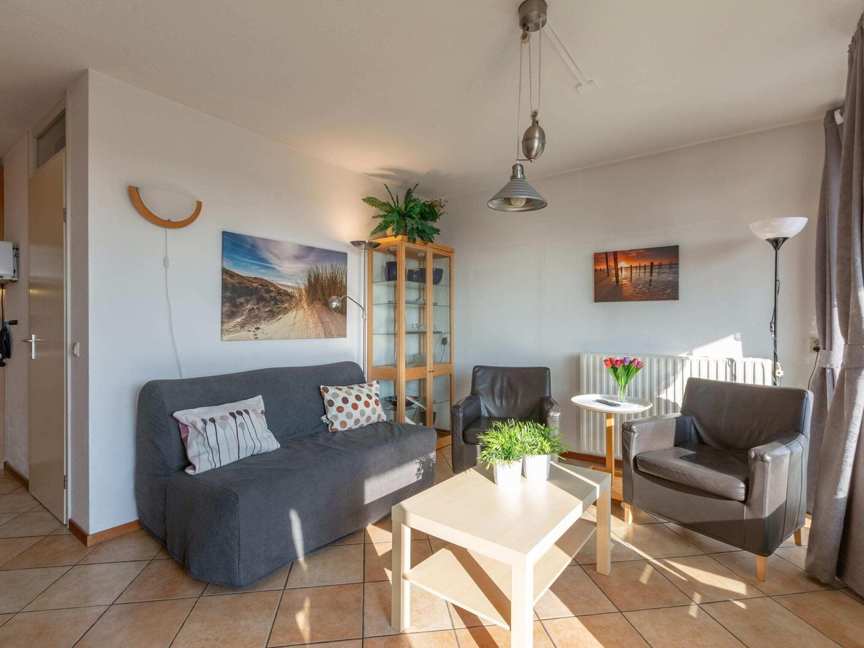 A living room with a grey sofa, a coffee table, a cabinet, and a chair. There is a painting on the wall and a plant on the cabinet.