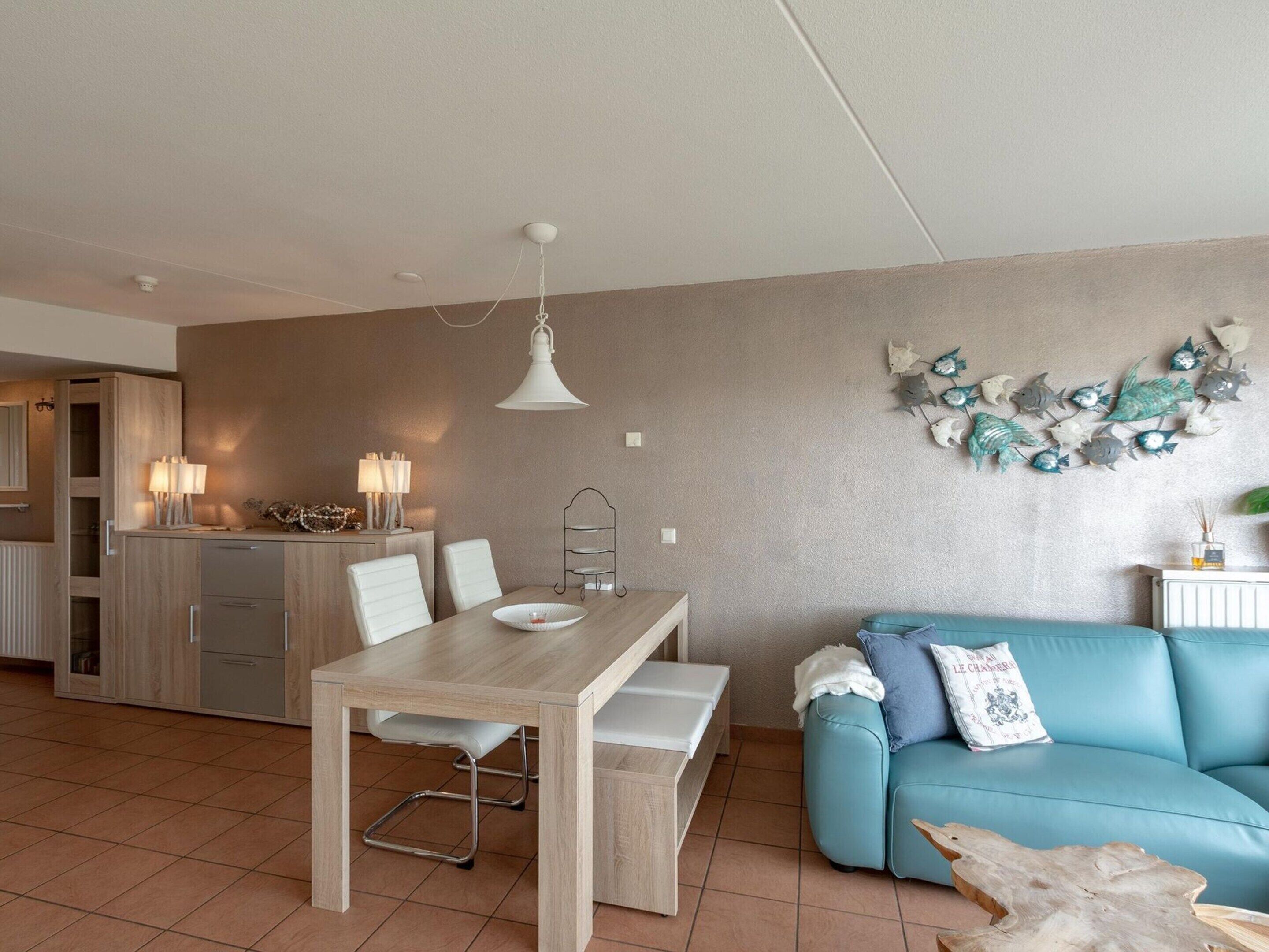 Een moderne woonkamer met een eettafel, een blauwe bank en een keuken op de achtergrond.