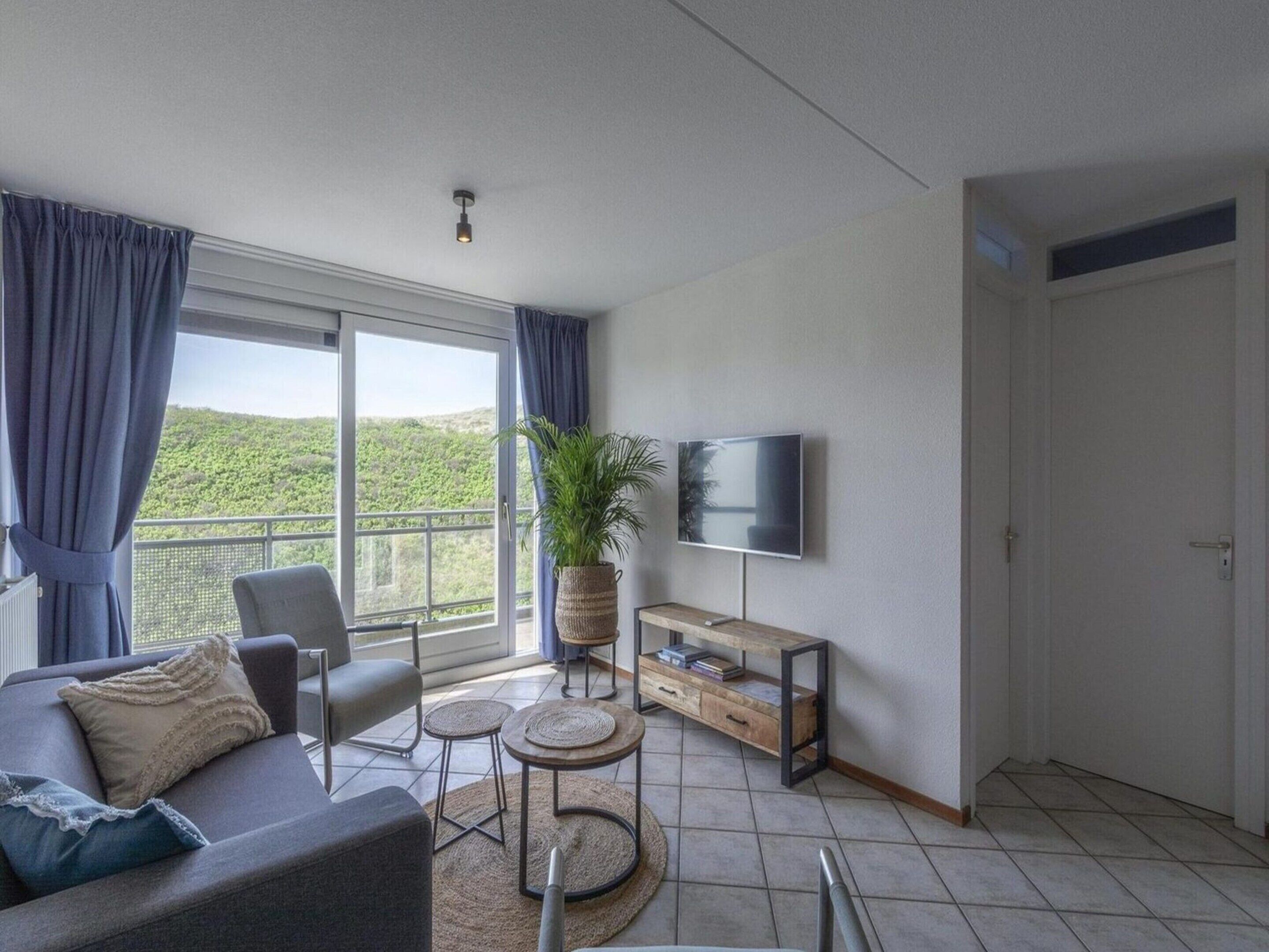 Una sala de estar moderna con un sofá, sillones, un televisor y un balcón con vistas a zonas verdes.