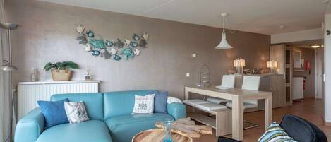 A modern living room with a blue sofa, a wooden coffee table, and a dining area with a wooden table and chairs.