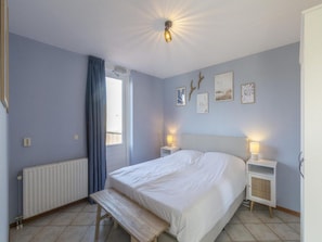 A bedroom with a bed, bedside tables, a bench, a radiator, and a window with curtains. - A Modern Wellness Holiday Apartment (Callantsoog)