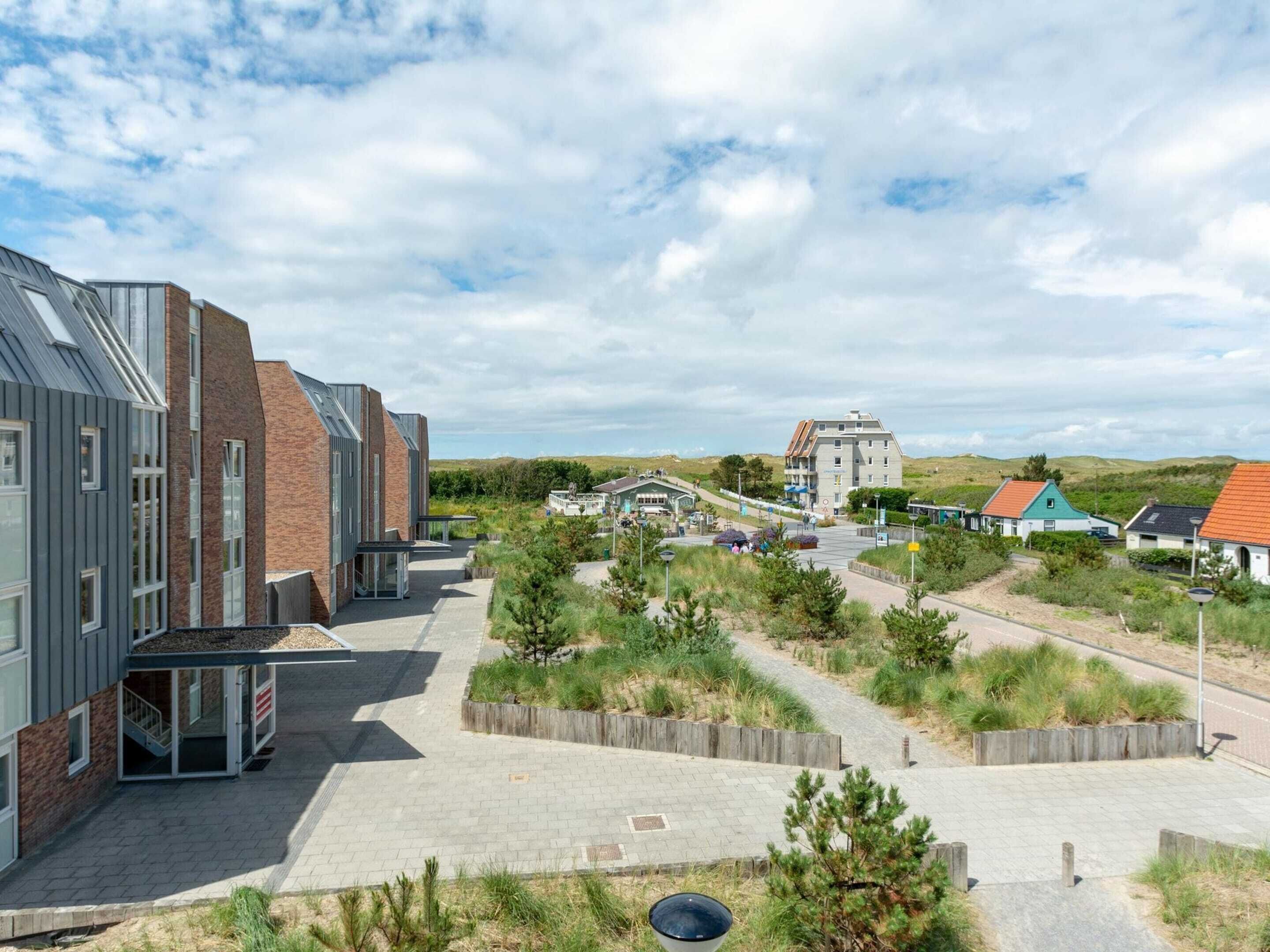 A modern building with a flat roof and a brick facade, surrounded by a landscaped area with pathways and small trees.