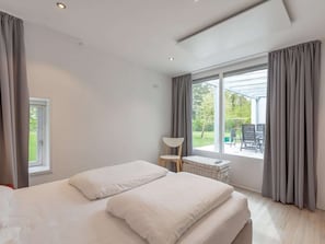 A modern bedroom with a large bed, a small side table, and a view of the outdoors.