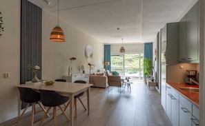 A modern kitchen with a built-in oven, a dining area with a white table and chairs, and a living area with a sofa and a coffee table.