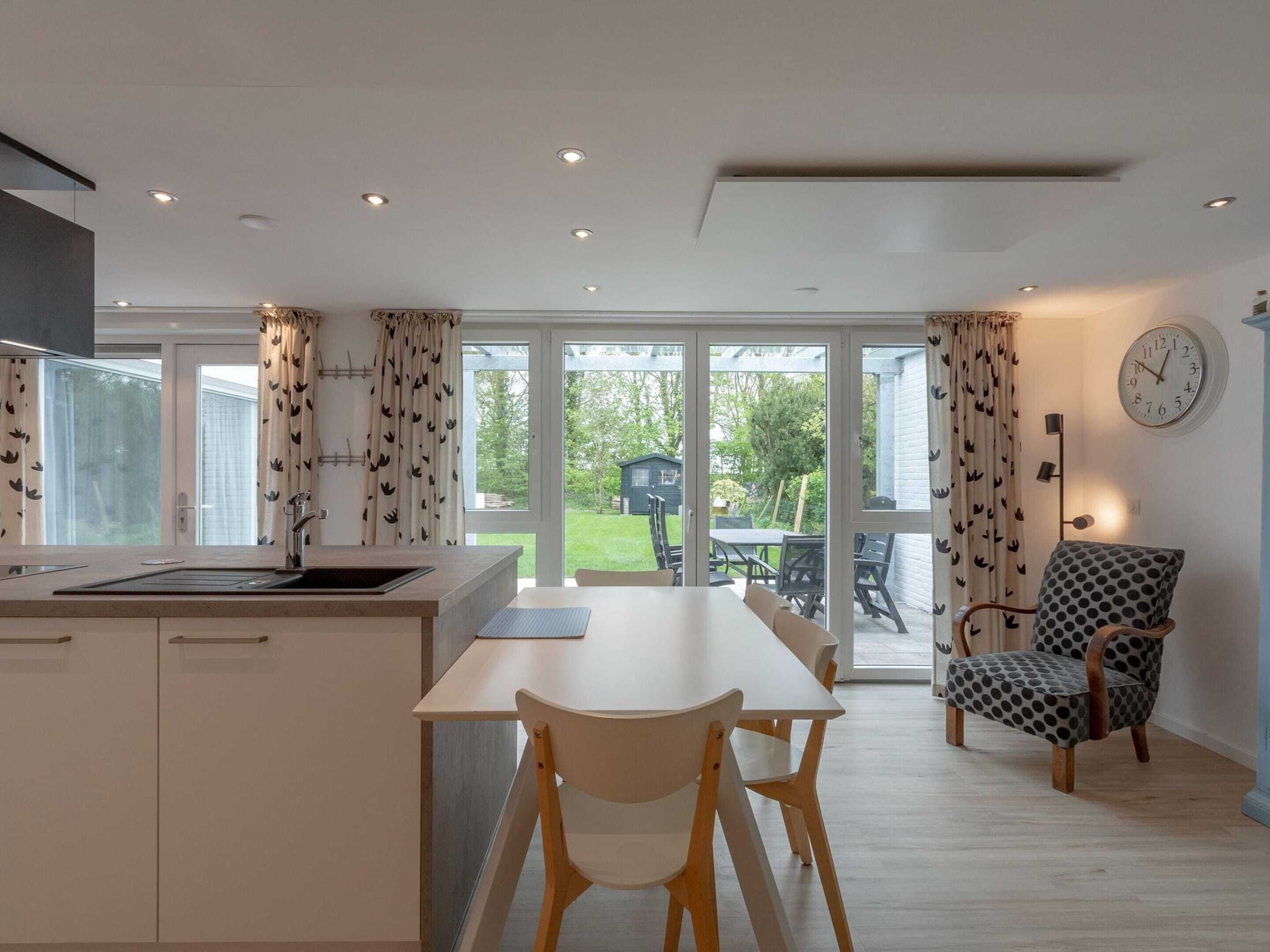 A modern kitchen with a dining area, large windows, and a view of the garden.