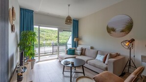 Uma sala de estar moderna com um sofá, mesa de centro e uma grande janela com vista para o verde.