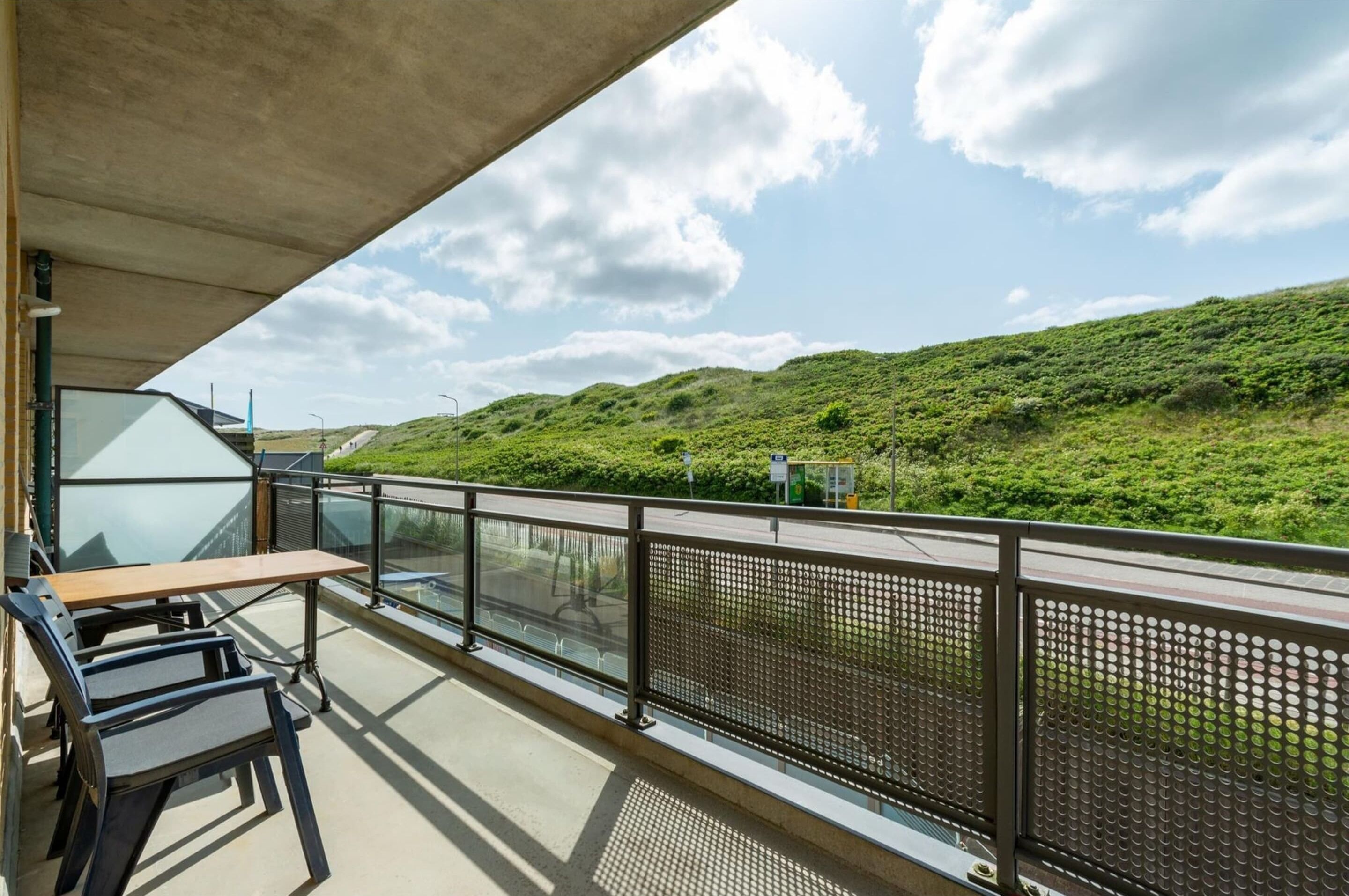 Ein Balkon mit Glasgeländer, der auf eine grüne Landschaft und eine Straße hinausblickt.