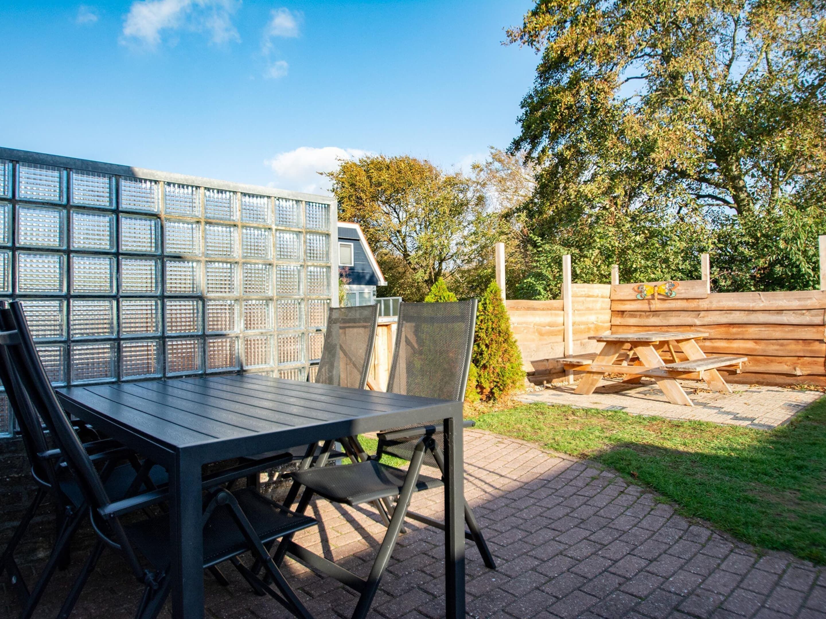An outdoor patio with a metal table and chairs, a wooden fence, and a grassy area.