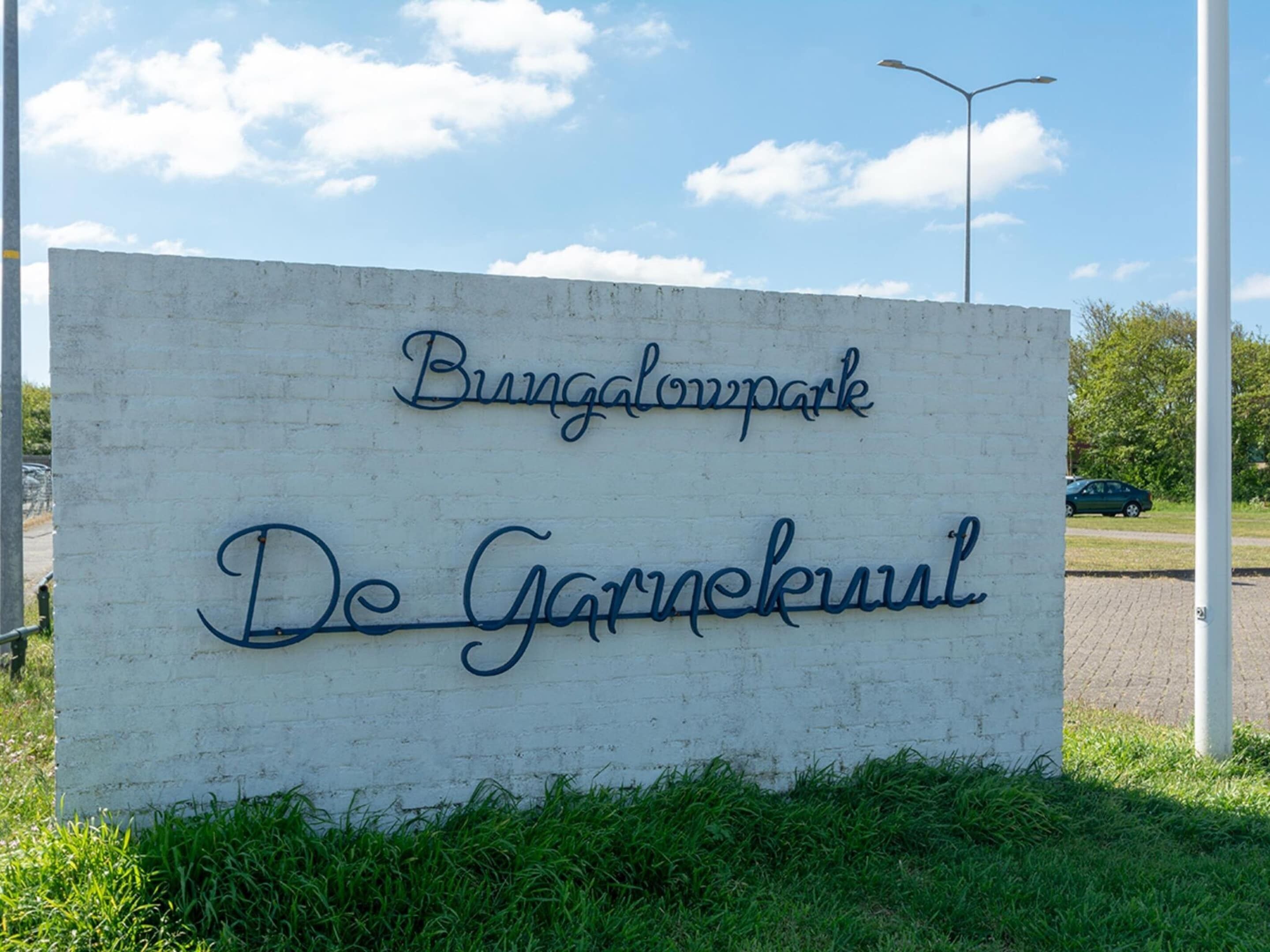 A sign for 'Bungalowpark De Garmenkuil' with a clear sky and grass in the foreground.